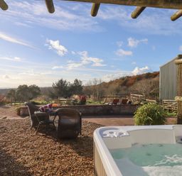 An outdoor patio area with a hot tub and wicker chairs overlooking a garden and trees at Sherway Dairy in Clyst Hydon near Bradninch