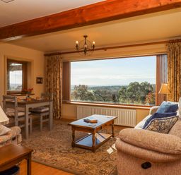 A living room with a sofa a coffee table a dining table and large window with a view at Sherway Dairy in Clyst Hydon near Bradninch