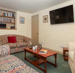 A sitting room with patterned sofas a wooden coffee table a wall-mounted television and shelves with books and DVDs at Sherway Shippen in Clyst Hydon near Bradninch