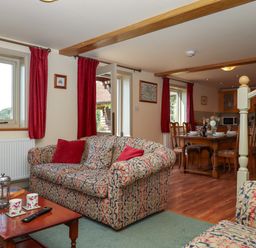 A living room with patterned sofas red cushions red curtains wooden dining table with chairs and kitchen area at Sherway Shippen in Clyst Hydon near Bradninch