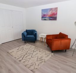 A room with a blue and orange armchair a white side table a floor lamp a painting on the wall and a rug on the floor at 69 Ffordd Y Meillion in Llanelli