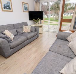 A living room with two gray sofas a television on a stand flowers on the stand and a sliding glass door showing a garden outside at Forbes C1 in Yarmouth