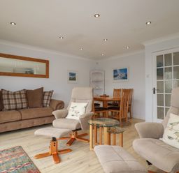 A living room with beige armchairs a brown sofa dining table and chairs and a glass side table at 3 The Bowling Green in St Just in Roseland near St Mawes
