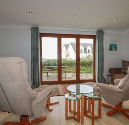 A living room with two armchairs a glass coffee table next to a sliding door at 3 The Bowling Green in St Just in Roseland near St Mawes