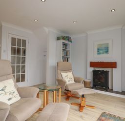 A sitting room with two armchairs a glass side table a bookshelf a wood stove and a television at 3 The Bowling Green in St Just in Roseland near St Mawes