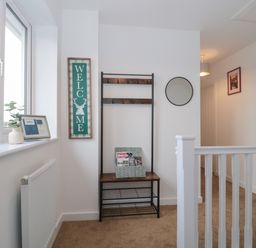 A hallway with a coat rack bench mirror and welcome sign at Cotswold Outlet Coach House in Tewkesbury
