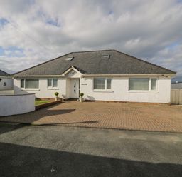 A white house with a grey tiled roof and paved driveway at The Gables in Tywyn