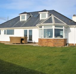 A white house with a gray roof and a patio table with chairs on a lawn at The Gables in Tywyn