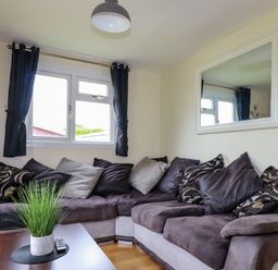 A living room with a sectional sofa and a table with a plant at Gwanda Tregolds near St Merryn