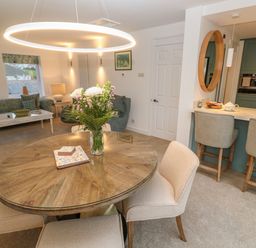 A dining area with a round wooden table and chairs next to a kitchen with bar stools and a living room with sofas at Fal View in Falmouth