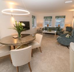 A living room with a round dining table with flowers on it and seating area with sofas and armchairs at Fal View in Falmouth