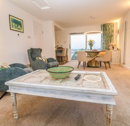 A living room with blue armchairs a white coffee table a round dining table with chairs and a wall mounted TV at Fal View in Falmouth