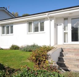The exterior of a white building with windows and a glass door with concrete stairs and garden at Trestar in Polzeath