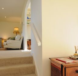 A carpeted staircase leading to a living room with an armchair a lamp and a dresser with a mirror and decor at Trestar in Polzeath