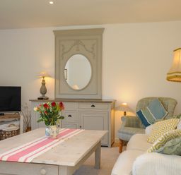 A living room with a sofa and armchair a wooden coffee table with flowers and a TV on a stand at Trestar in Polzeath