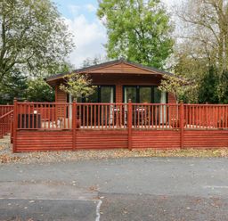 A wooden cabin with a red painted deck and railings surrounded by trees at Somerford Lodge Langdale 7 White Cross Bay near Windermere