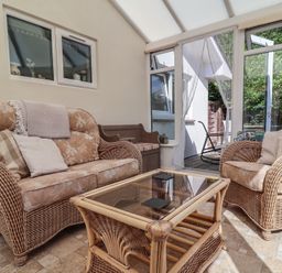 A conservatory with wicker furniture and a glass table at Little Willesleigh in Goodleigh near Barnstaple