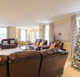 A living room with leather sofas a decorated Christmas tree and floral curtains at The Little House in Horning