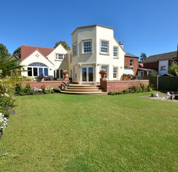 A garden with a lawn and flowers in front of a white house with red roof tiles at The Little House in Horning