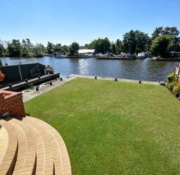A garden with grass lawn and flower pots overlooking a river with boats at The Little House in Horning