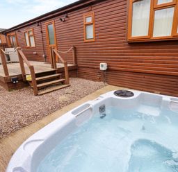 An outdoor hot tub next to a wooden deck and brown wooden building at Butterfly Lodge in Tunstall near Catterick North Yorkshire