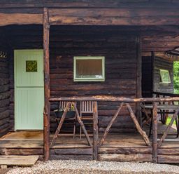 A wooden porch with rustic railing two wooden chairs and a small table at The Log Cabin in Sheldon Blackdown Hills