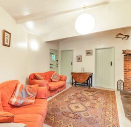 A living room with orange sofas a patterned rug a brick fireplace and wooden doors at The Log Cabin in Sheldon Blackdown Hills