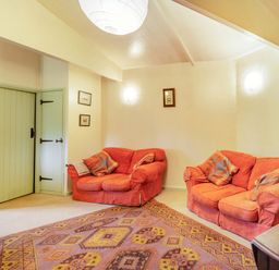 A living room with two orange sofas an oriental rug and green doors at The Log Cabin in Sheldon Blackdown Hills