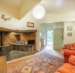 A living room with orange sofas a patterned rug a brick fireplace and wood stove at The Log Cabin in Sheldon Blackdown Hills