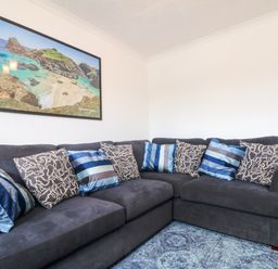 A corner sofa with blue and patterned cushions in a living room with a framed picture on the wall at Savoy View in Mullion