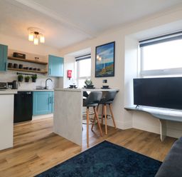 A kitchen and dining area with blue cabinets stools and a TV near windows at Savoy View in Mullion