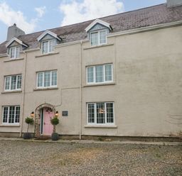 A large house with multiple white windows and a pink front door with two potted plants at Norchard Farm House in Redberth near St Florence