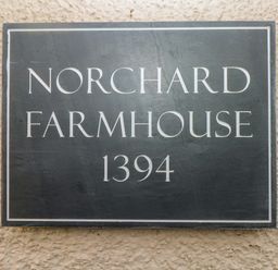 A sign on a textured wall reading Norchard Farmhouse 1394
