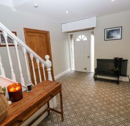 An entrance hallway with a white door a wooden table by white stairs and wooden doors at Norchard Farm House Redberth near St Florence