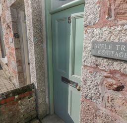 A green front door with number 5 and a sign reading apple tree cottage on a stone wall at Apple Tree Cottage in Gweek