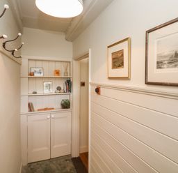 A hallway with a built-in shelving unit a row of coat hooks and framed pictures on the wall at Apple Tree Cottage in Gweek