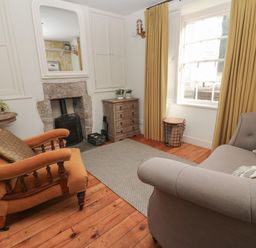 A living room with an orange armchair a gray sofa a stone fireplace wooden floor and a window with yellow curtains at Apple Tree Cottage in Gweek