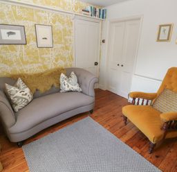 A sitting room with a grey sofa and a mustard armchair on wood floors at Apple Tree Cottage in Gweek