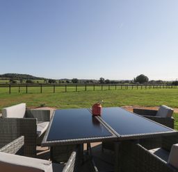 An outdoor patio table with chairs overlooking a fenced grassy field at Leadon View Willow in Upleadon near Newent