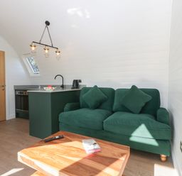 A small living room with a green sofa, wooden coffee table, and kitchen area at Leadon View Willow in Upleadon near Newent