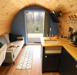 A compact wooden interior with a small kitchen area and a gray sofa in a curved cabin at Hobhole in Keal Cotes near East Kirkby
