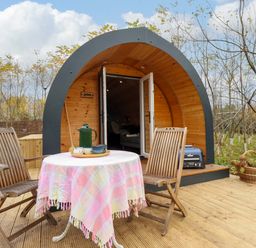 A wooden outdoor deck with a round table covered with a cloth and two wooden chairs in front of a curved wooden cabin at Hobhole in Keal Cotes near East Kirkby