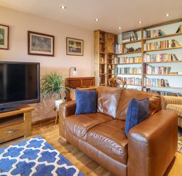 A living room with a brown leather sofa blue pillows a television wooden shelves filled with books and framed pictures on the wall at Hendre in Blaenau Ffestiniog