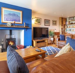 A living room with leather sofas a wooden coffee table a fireplace with a wood burning stove a television and bookshelves at Hendre in Blaenau Ffestiniog