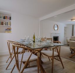 A dining area with a glass table set for six with wooden chairs next to a living room with armchairs and a fireplace at 47 Church Street in Lyme Regis