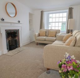A living room with two beige sofas cushions fireplace TV and flowers on a table at 47 Church Street in Lyme Regis
