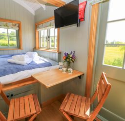 A sleeping area with a bed and table at Goose Whistle Hut in Foxham