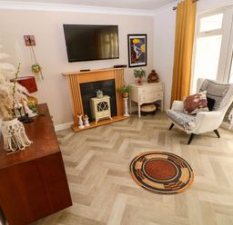 A living room with a TV above a fireplace an armchair and a round rug at Alban Road in Llanelli
