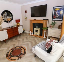 A living room with a wall-mounted tv above a fireplace and a sideboard with decorations at Alban Road Llanelli