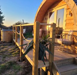 A wooden cabin with a small deck with two chairs and a hot tub outside surrounded by grass at Holbein in Matlock